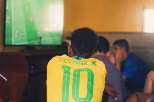 A soccer fan wearing a jersey sits in front of his TV and anxiously watches the game