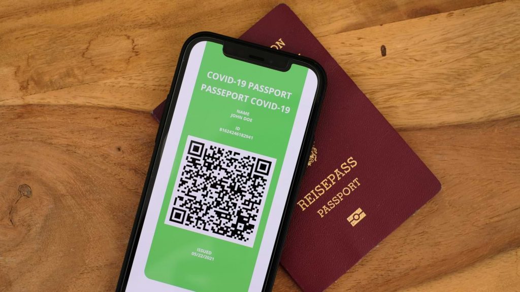 A physical passport next to a COVID-19 passport app on a smartphone.