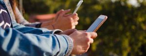 Two people using their cell phones side by side.