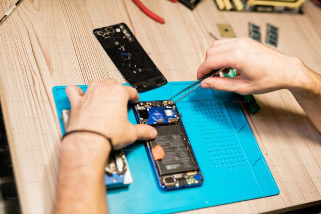 Hands repairing an opened smartphone on an electronics workbench