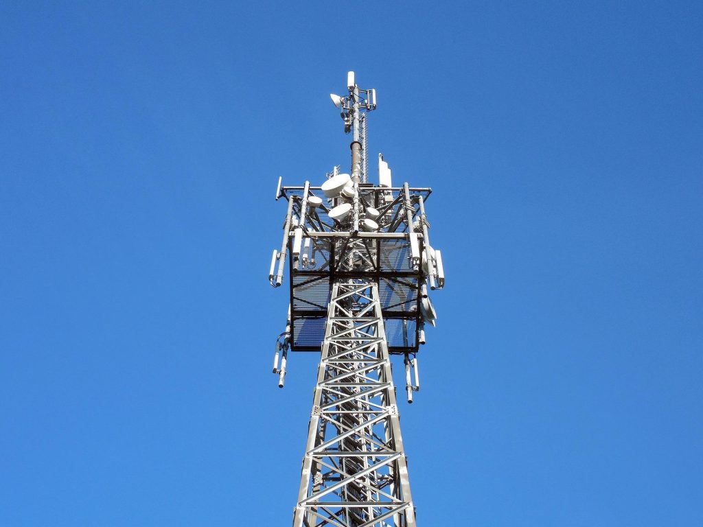 Tour de télécommunications équipée de plusieurs antennes et paraboles sous un ciel bleu.