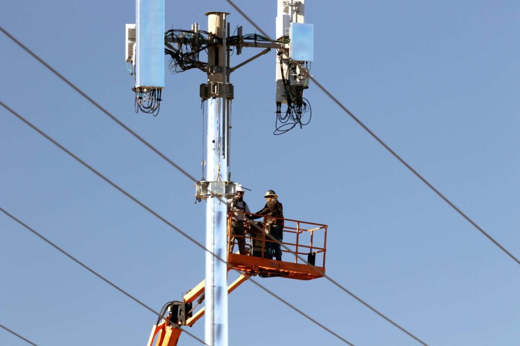 Deux techniciens sur une nacelle élévatrice interviennent sur les équipements d'un support d'antennes cellulaires.