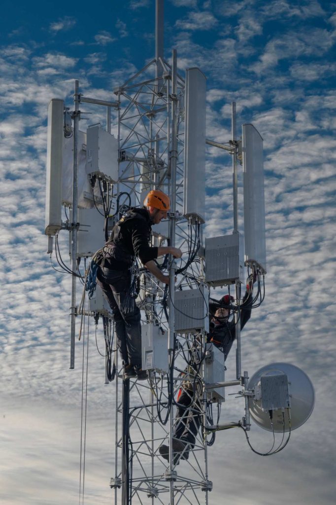 Deux techniciens équipés de harnais travaillent sur un pylône de télécommunications comportant plusieurs antennes.
